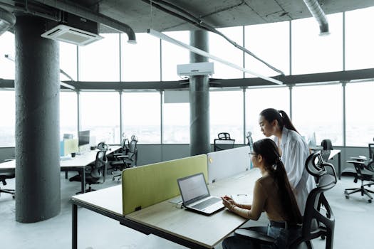 Two Asian women collaborating in a modern office environment focused on teamwork and innovation.